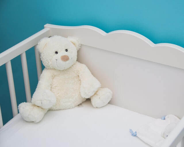 En hvid babyseng med en bamse i, som står op af en blå væg